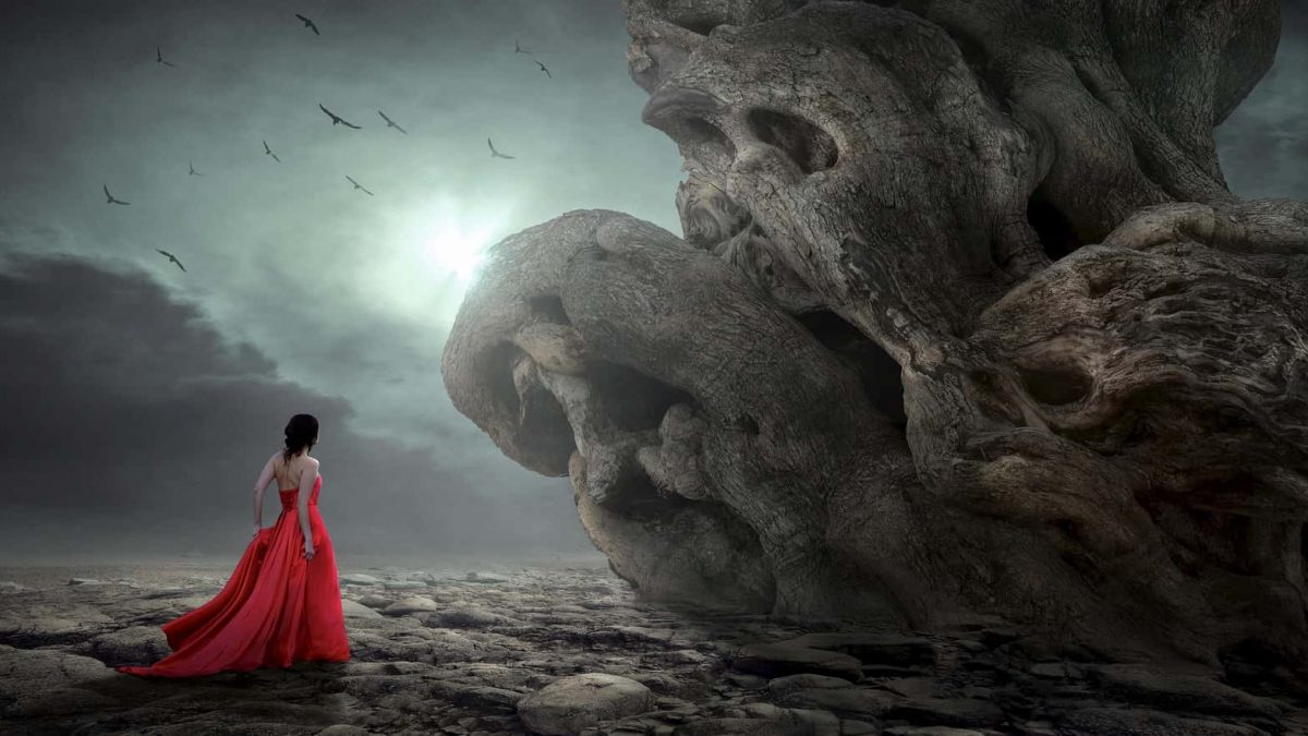 Une femme portant une robe de soirée rouge fait face à des rochers semblables à des cranes de mort dans un paysage sombre